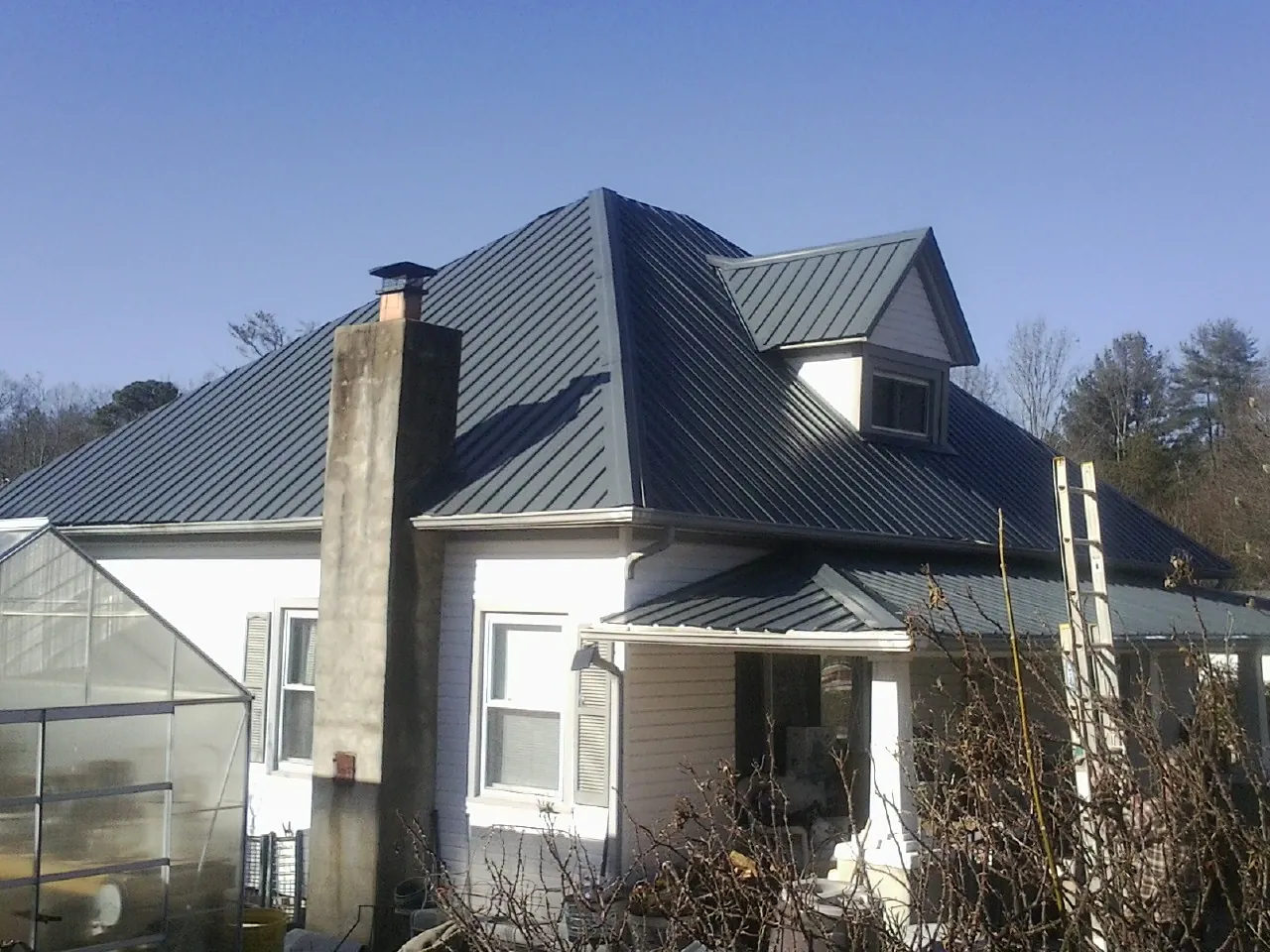 Dark blue standing seam metal roof on a white farmhouse with dormer — Slate & Tile Roof Repair by Roofing Brothers in Sherrill
