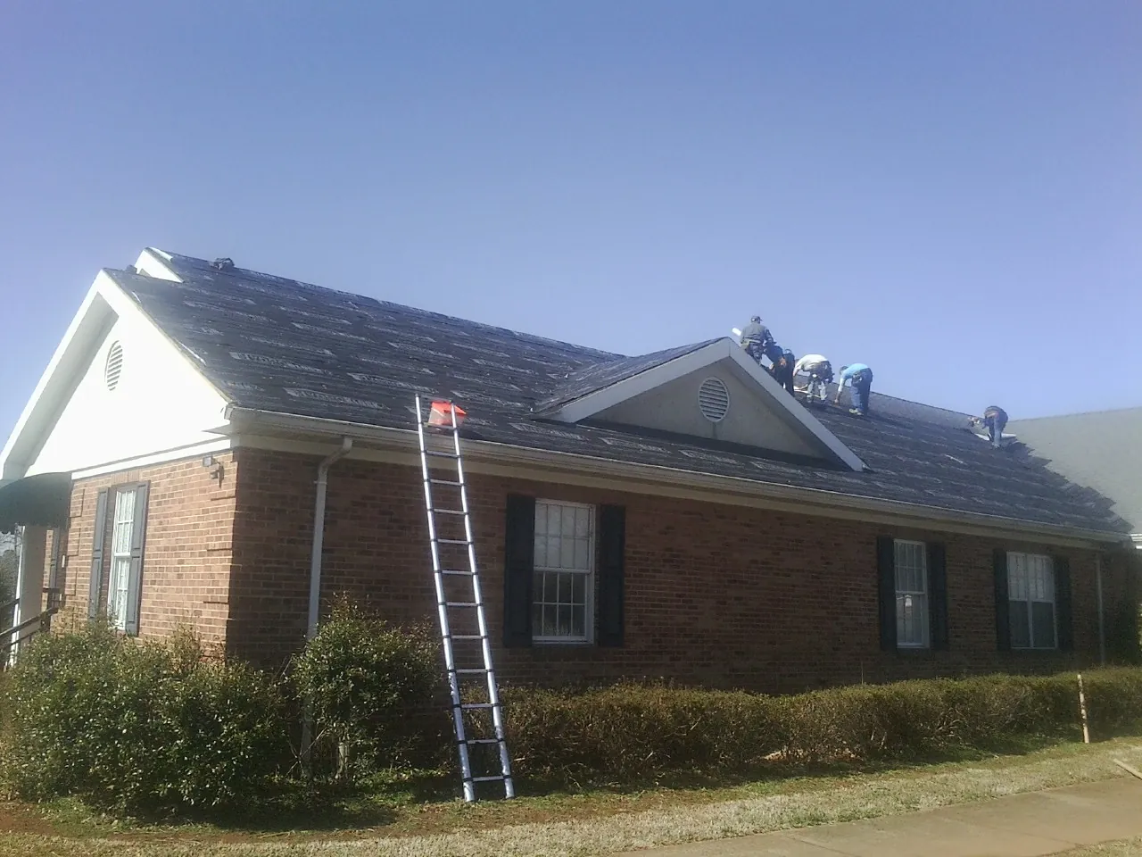 Crew tearing shingles off a brick ranch roof with a ladder set — Metal Roof Repair work by our crew in Sherrill