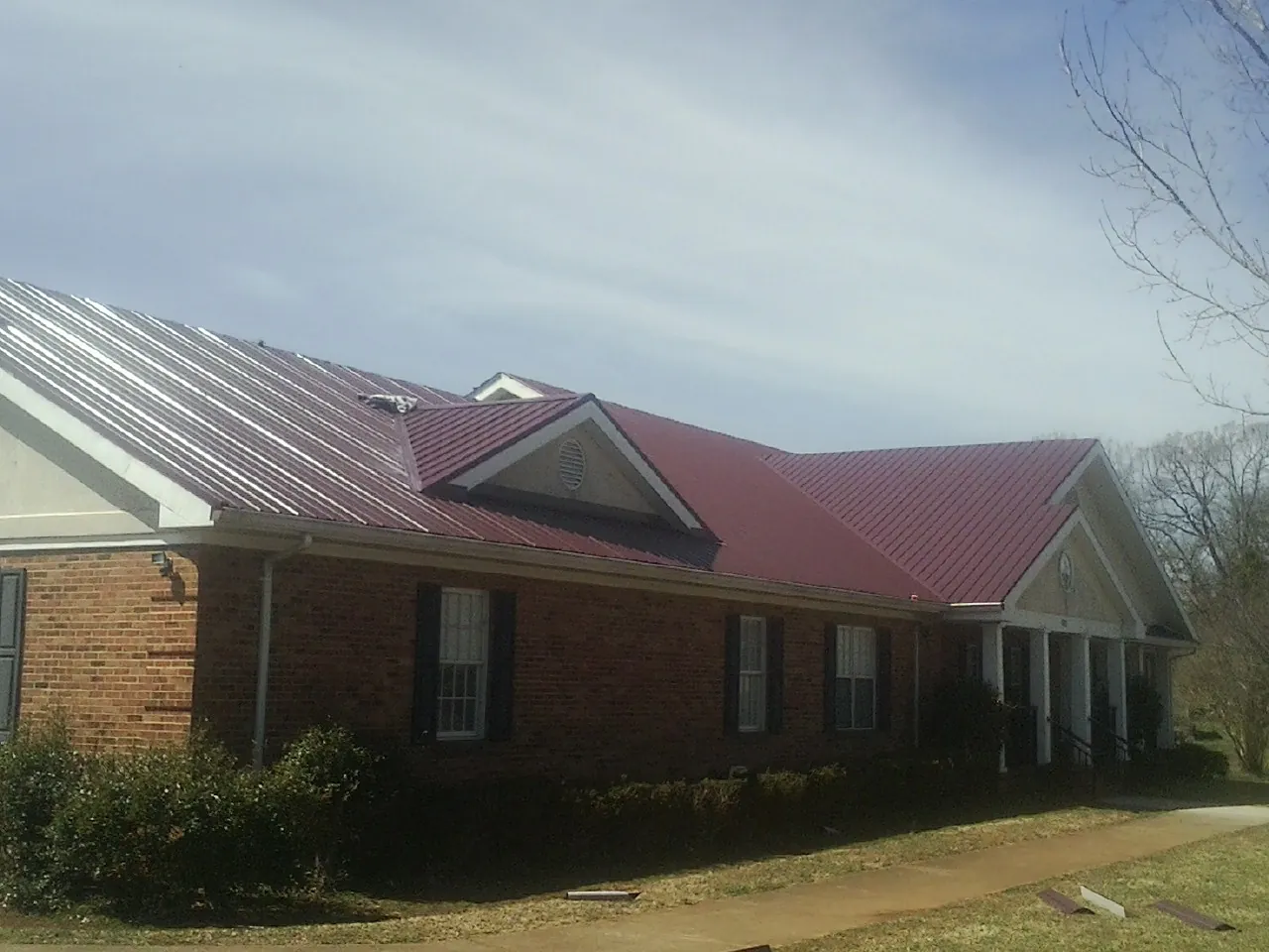 Red metal roof with gabled entries on a long brick building, from a Hail Damage Roof Repair job in Sherrill