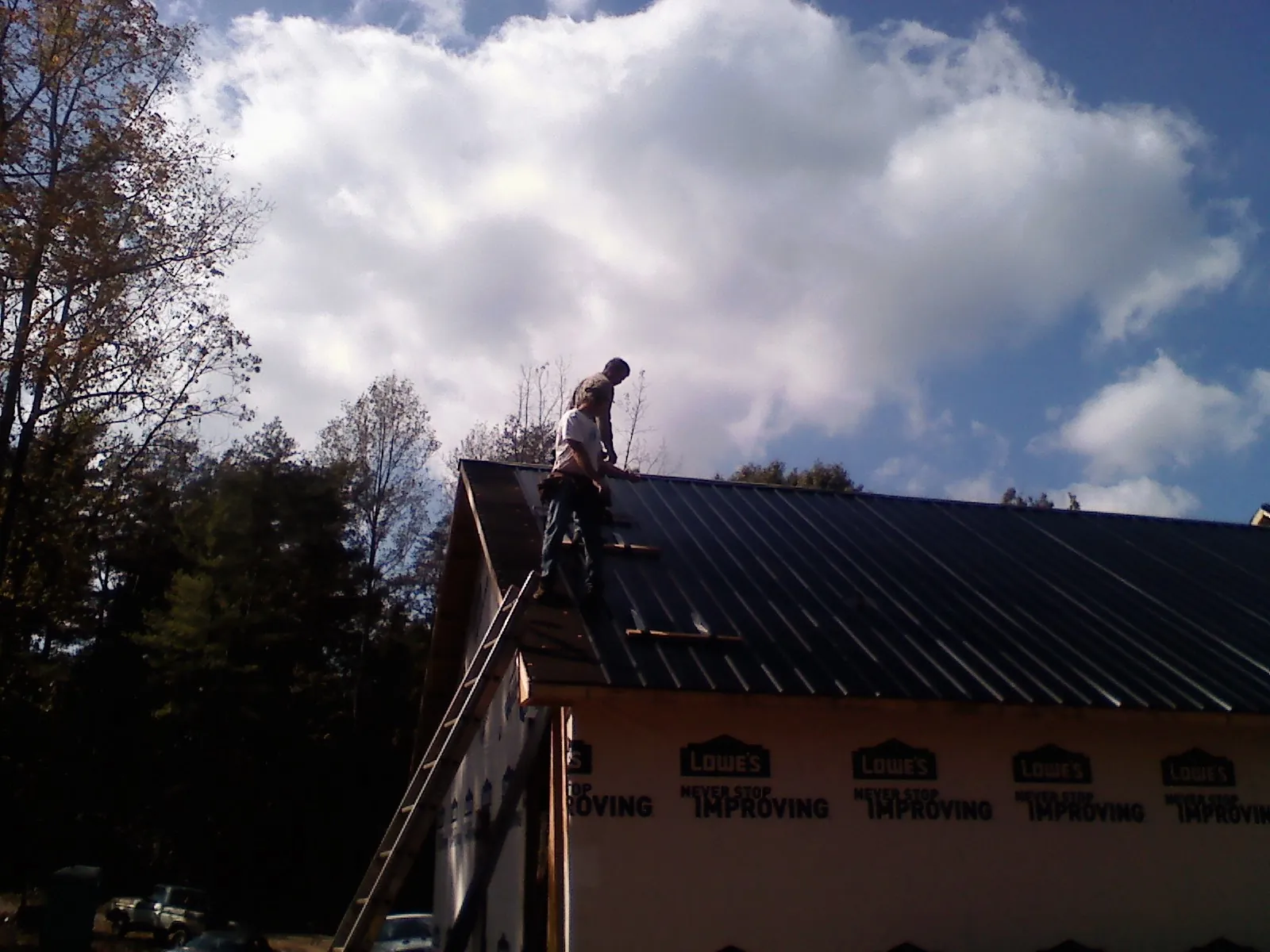 Roofer fastening dark metal panels high against a cloudy sky, from a Roof Inspection job in Sherrill