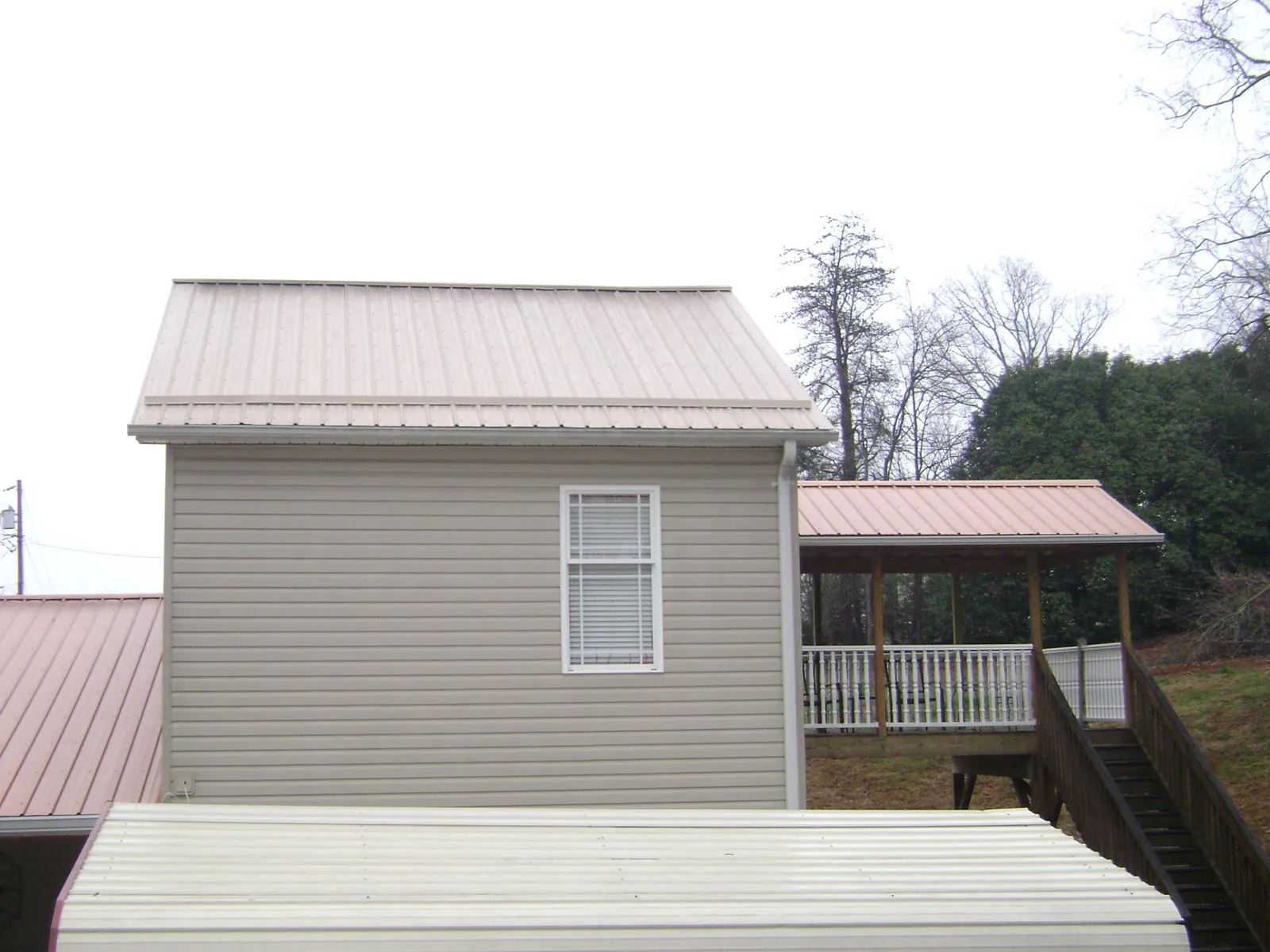 Tan metal roofs on a two story addition and attached porch, from a Roof Replacement job in Sherrill